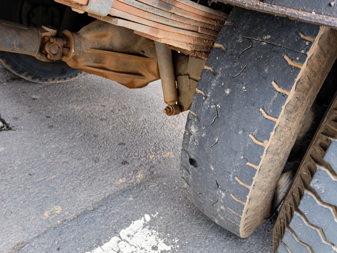 Close mostra pneu de caminhão com desgaste acentuado e rachaduras na borracha, evidenciando más condições de conservação. A imagem destaca a importância da manutenção dos veículos de carga para a segurança no trânsito.
