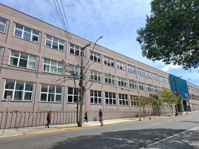 Fachada da FSG Centro Universitário, na Rua Marechal Floriano, com trechos do meio-fio pintados de amarelo e cones sinalizando a restrição de estacionamento. Pedestres circulam pela calçada.