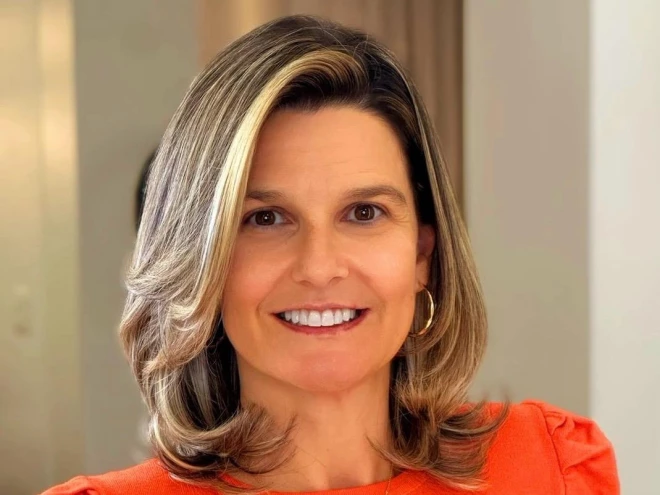 Vanessa da Silva, promotora de Justiça Eleitoral, sorri para a câmera em um retrato. Ela tem cabelos castanhos e loiros na altura dos ombros, usa brincos e veste uma blusa laranja, em ambiente interno.