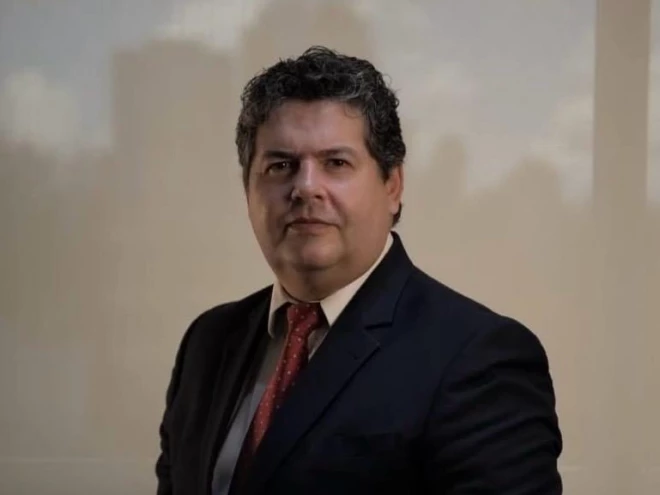 O advogado Giancarlo Fontoura Donato usando terno escuro, camisa branca e gravata vermelha. Com expressão séria e postura formal, aparece diante de um fundo neutro.